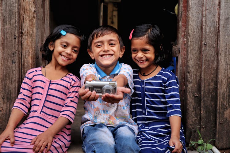 Smiling Boy Sitting Between Girls Holding Out Camera