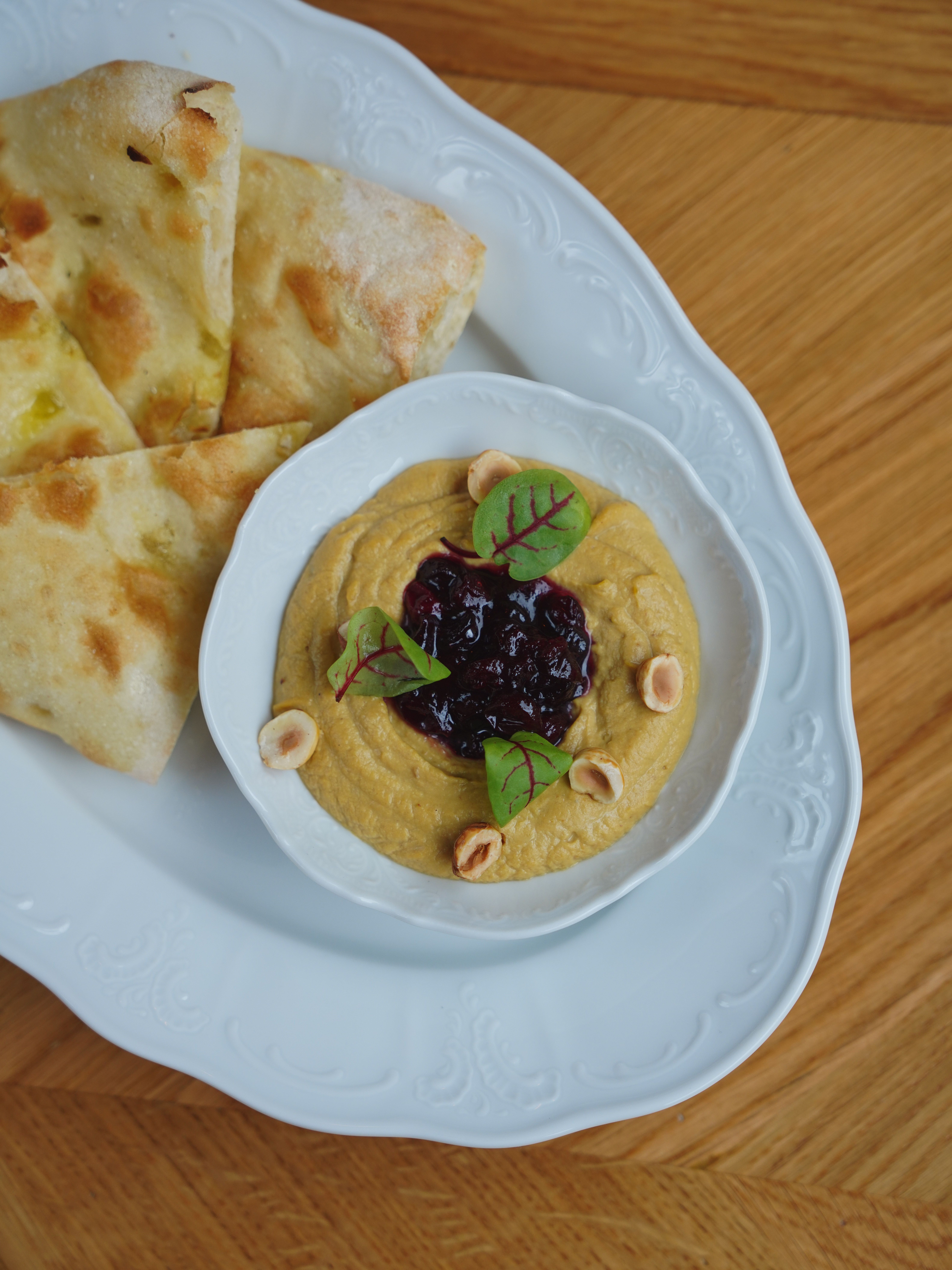 Hummus topped with berries and nuts served with pita bread on a white plate.