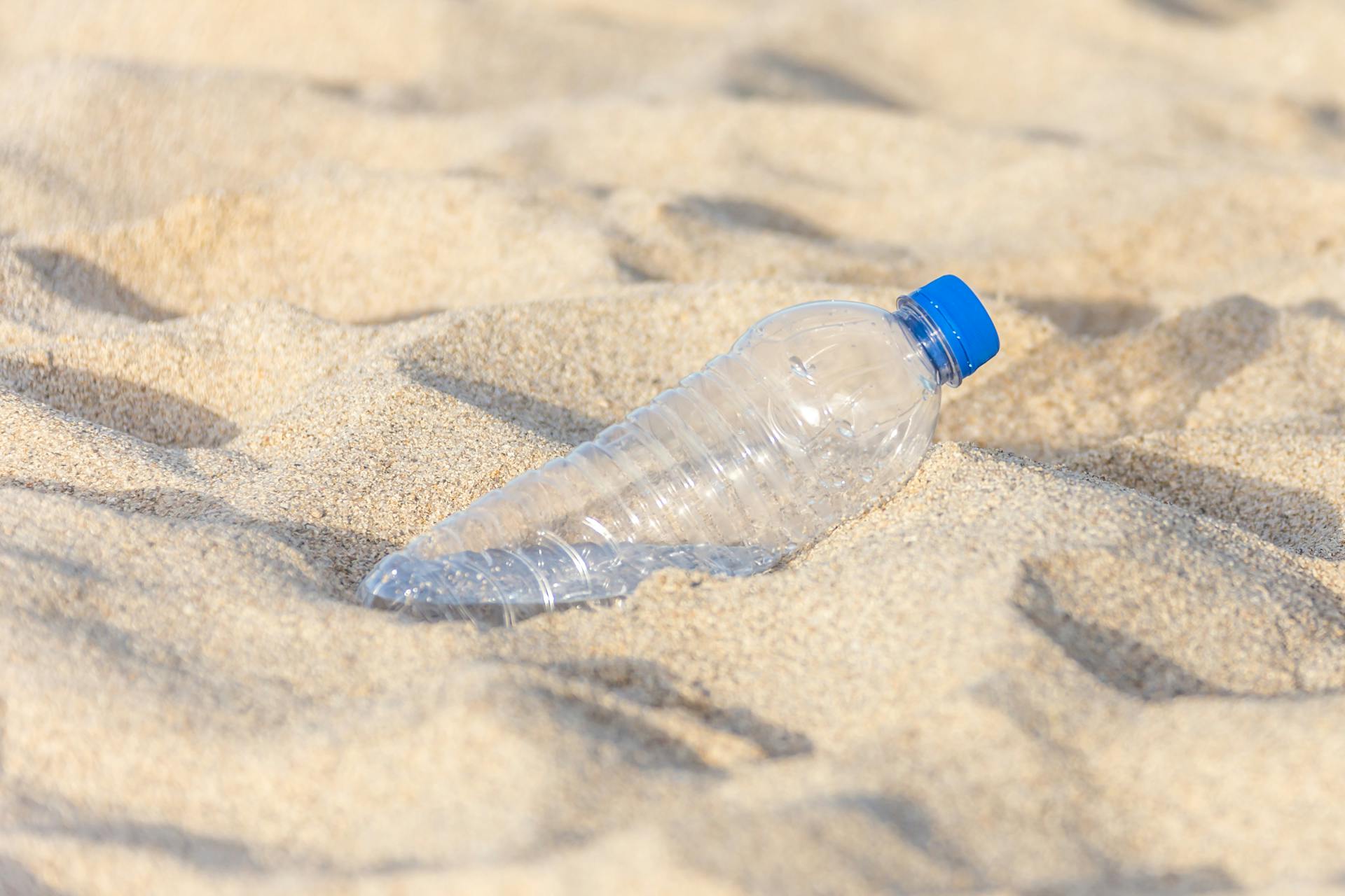 Plastic bottle on sandy beach highlighting pollution and environmental impact.