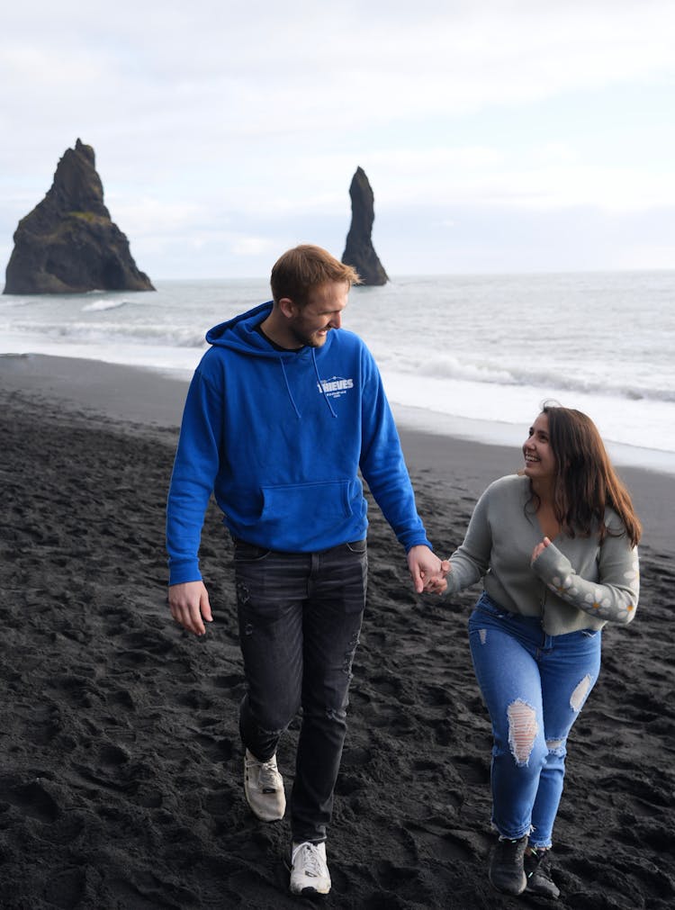 A Couple Walking On The Beach With Black Sand