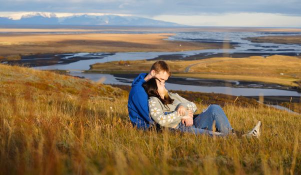 A couple embraces on a hillside overlooking a beautiful Icelandic landscape in autumn.