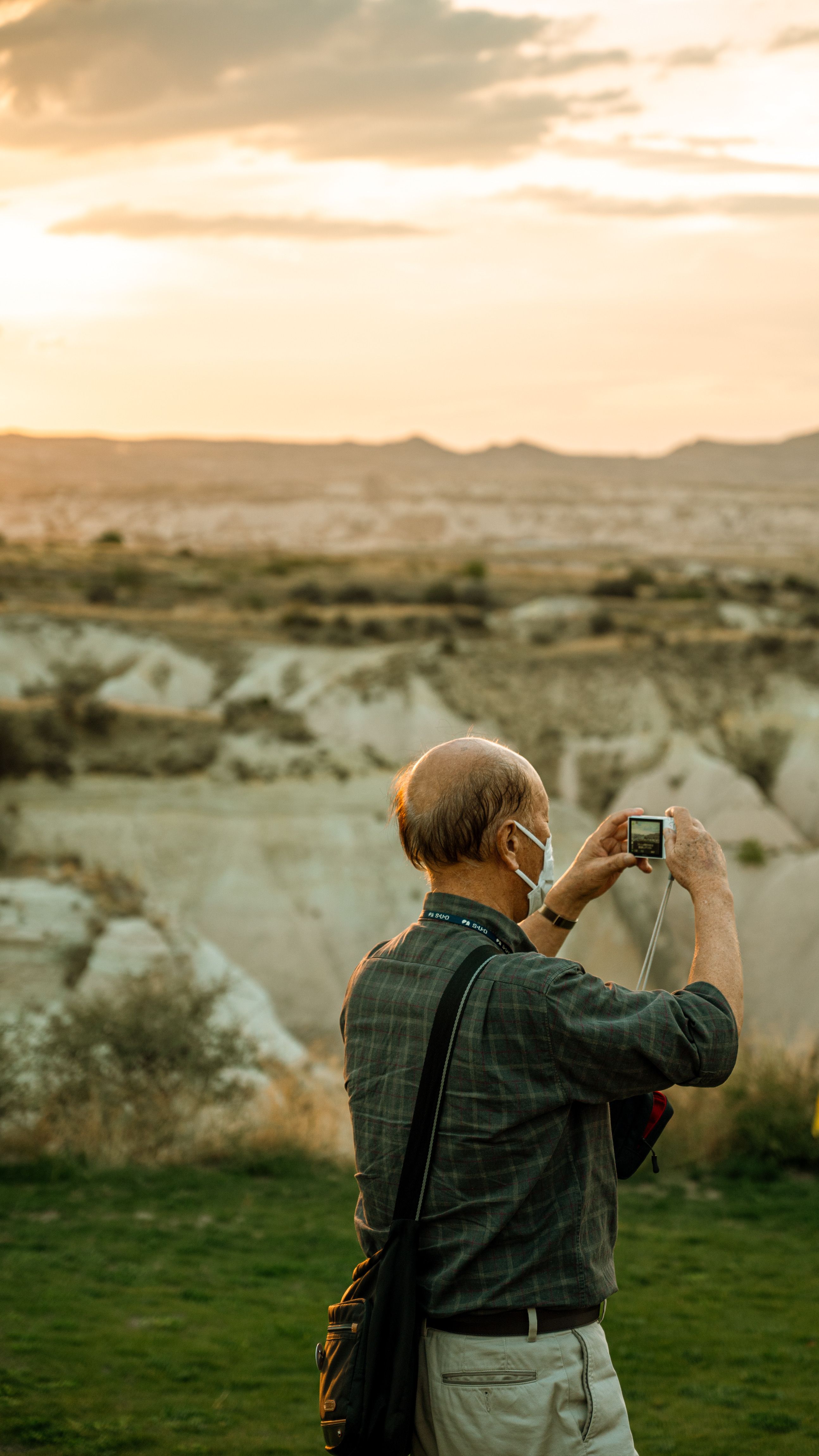Senior man photographing scenic countryside view during golden hour.