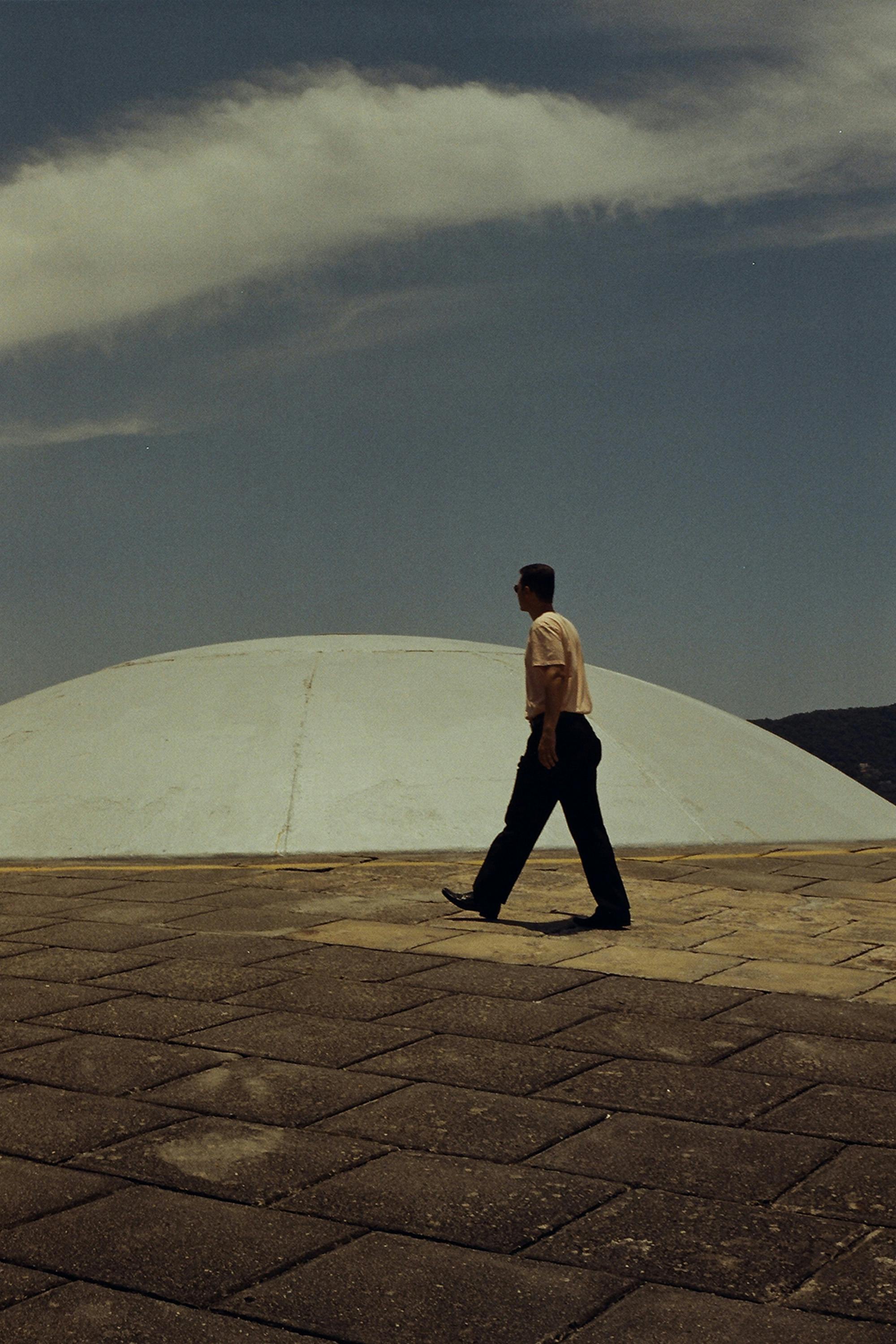 一名男子走在未来派圆顶结构旁的石板路上，天空晴朗