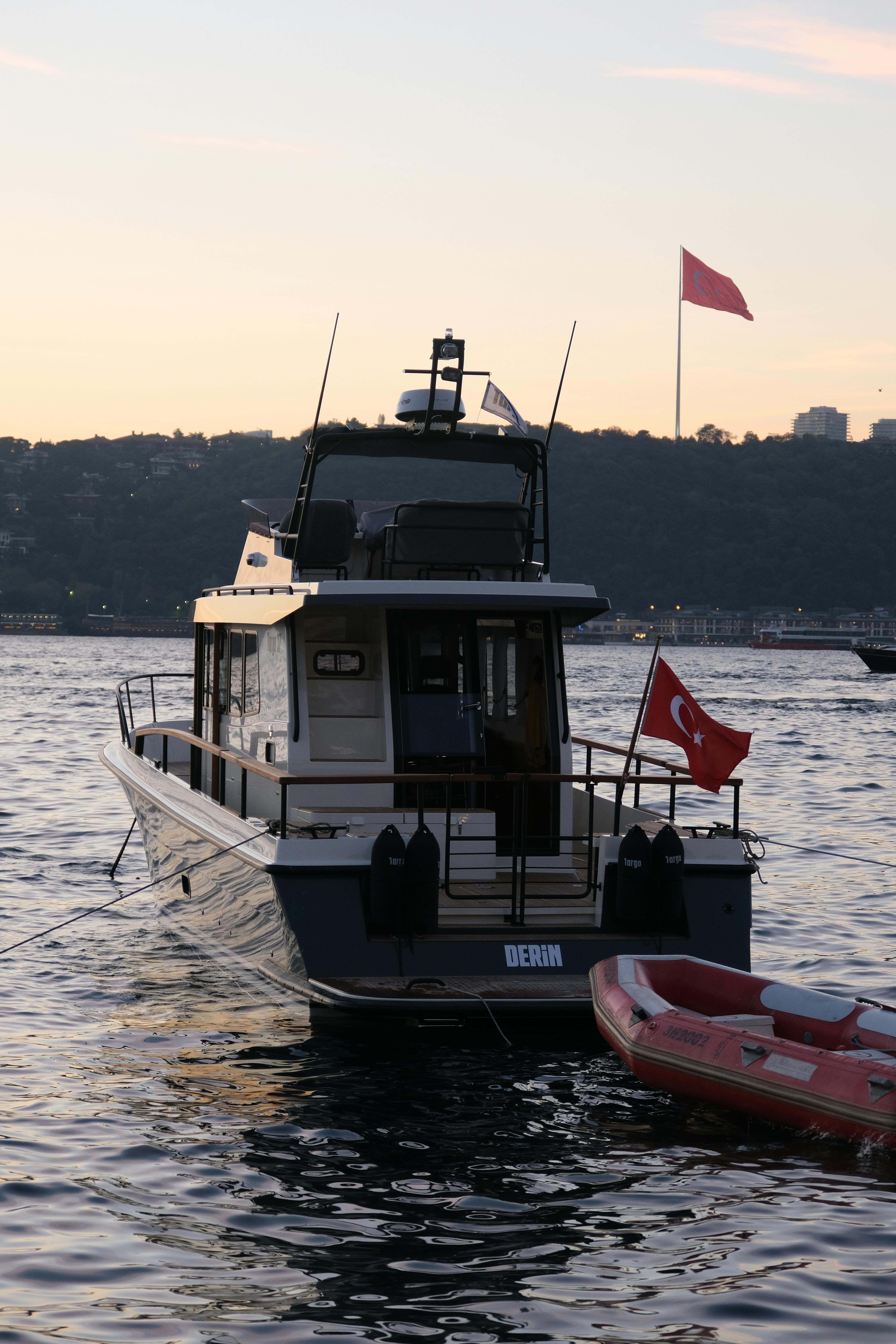 Motorboat with Turkish flags moored on Istanbul's scenic shoreline during sunset, featuring a calm sea.