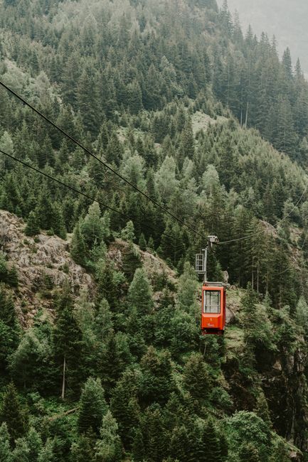 Vibrant red cable car traverses lush green mountains, offering breathtaking scenic views.