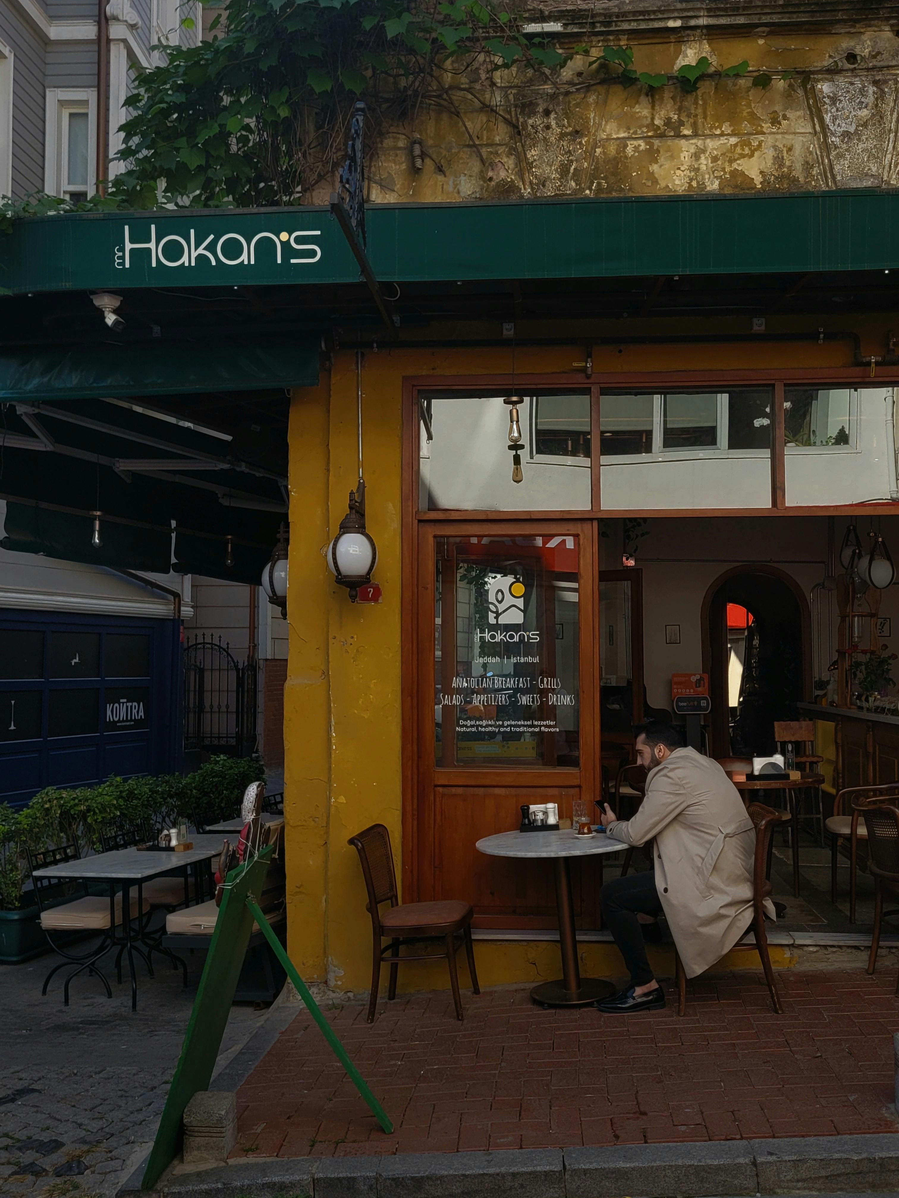 Man in Coat Sitting by Cafe Table on Sidewalk