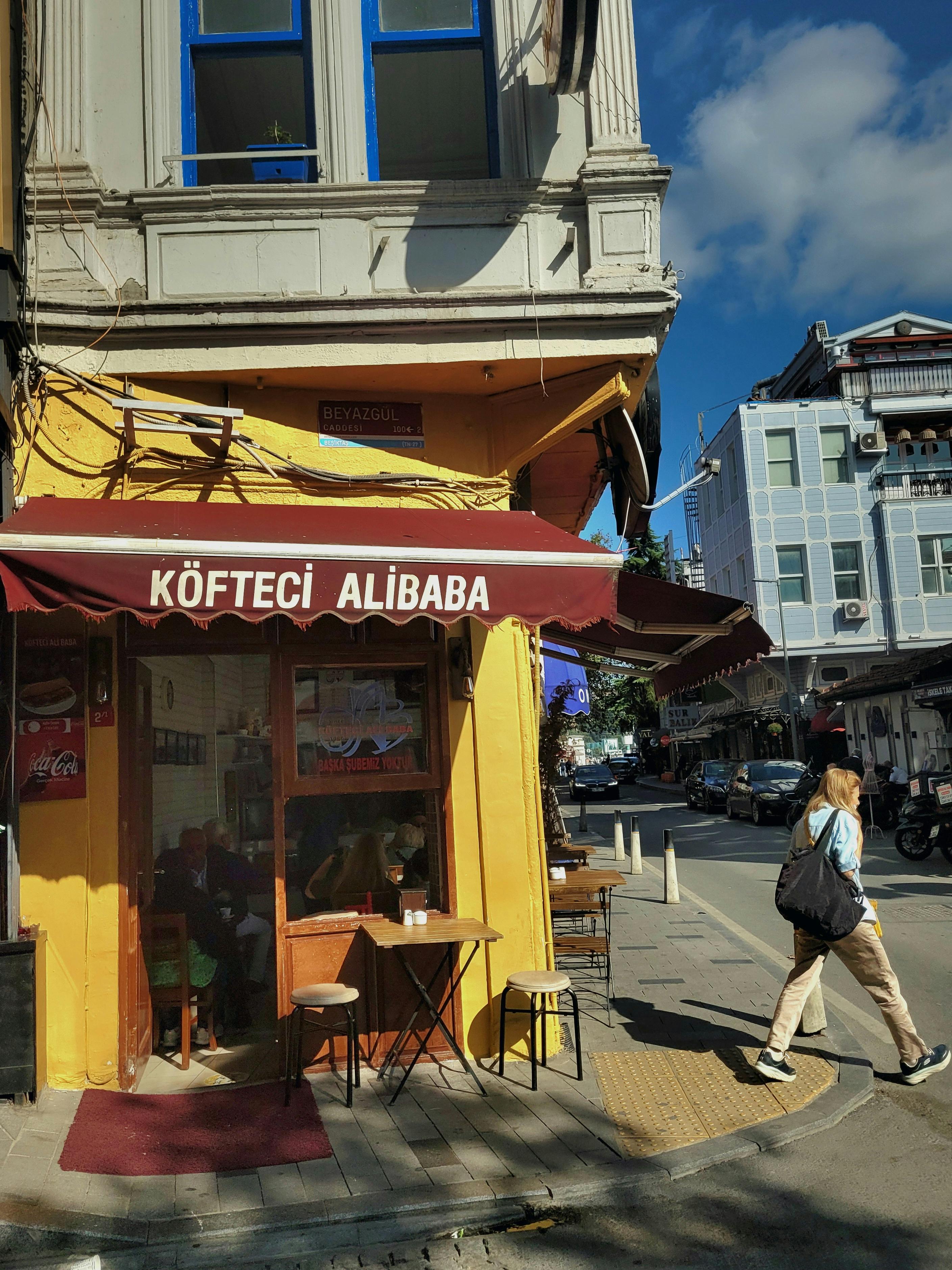 Woman walking past Köfteci Alibaba on a sunny urban street. Capturing the essence of Turkish city life.