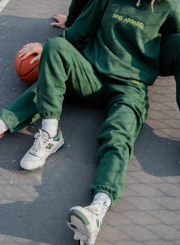 Person in green tracksuit sitting with basketball on urban court.