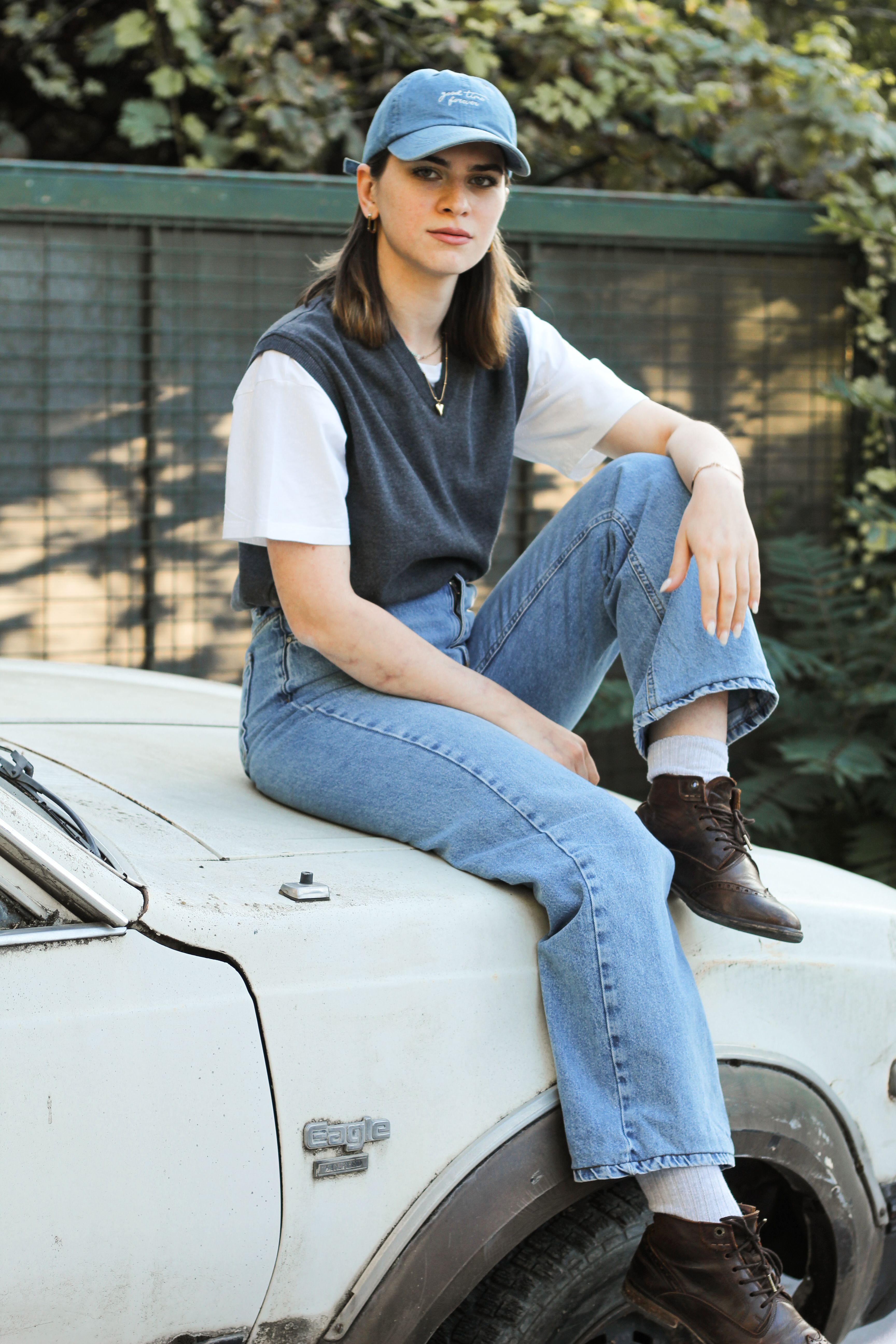 Woman in Cap and Vest Sitting on Car · Free Stock Photo