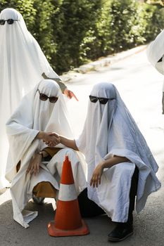 Playful Halloween scene with costumed ghosts shaking hands outdoors in daylight.