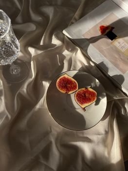 Figs on a plate with crystal glass against a silk backdrop in sunlight.