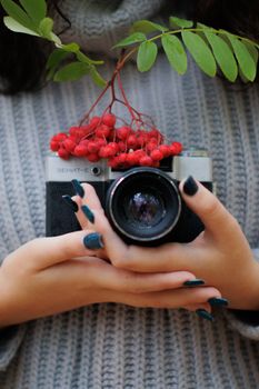 Close-up of a woman holding a vintage camera adorned with rowanberries and leaves.