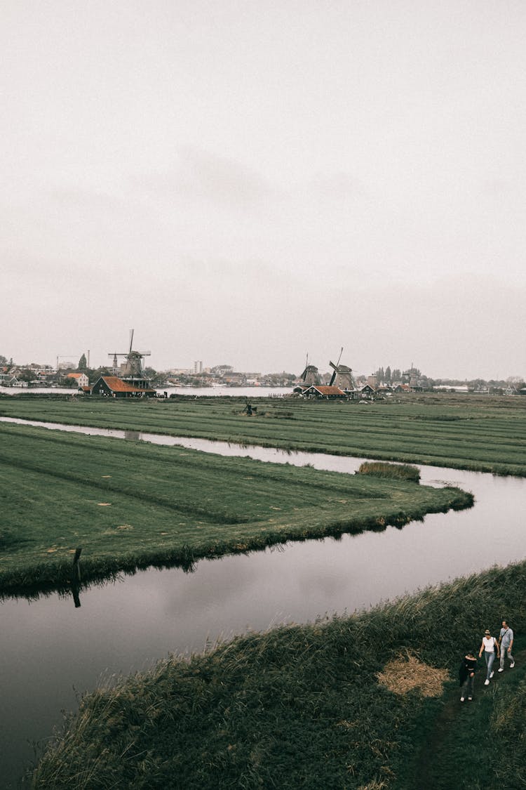 Canal On Field With Windmills Behind In Village