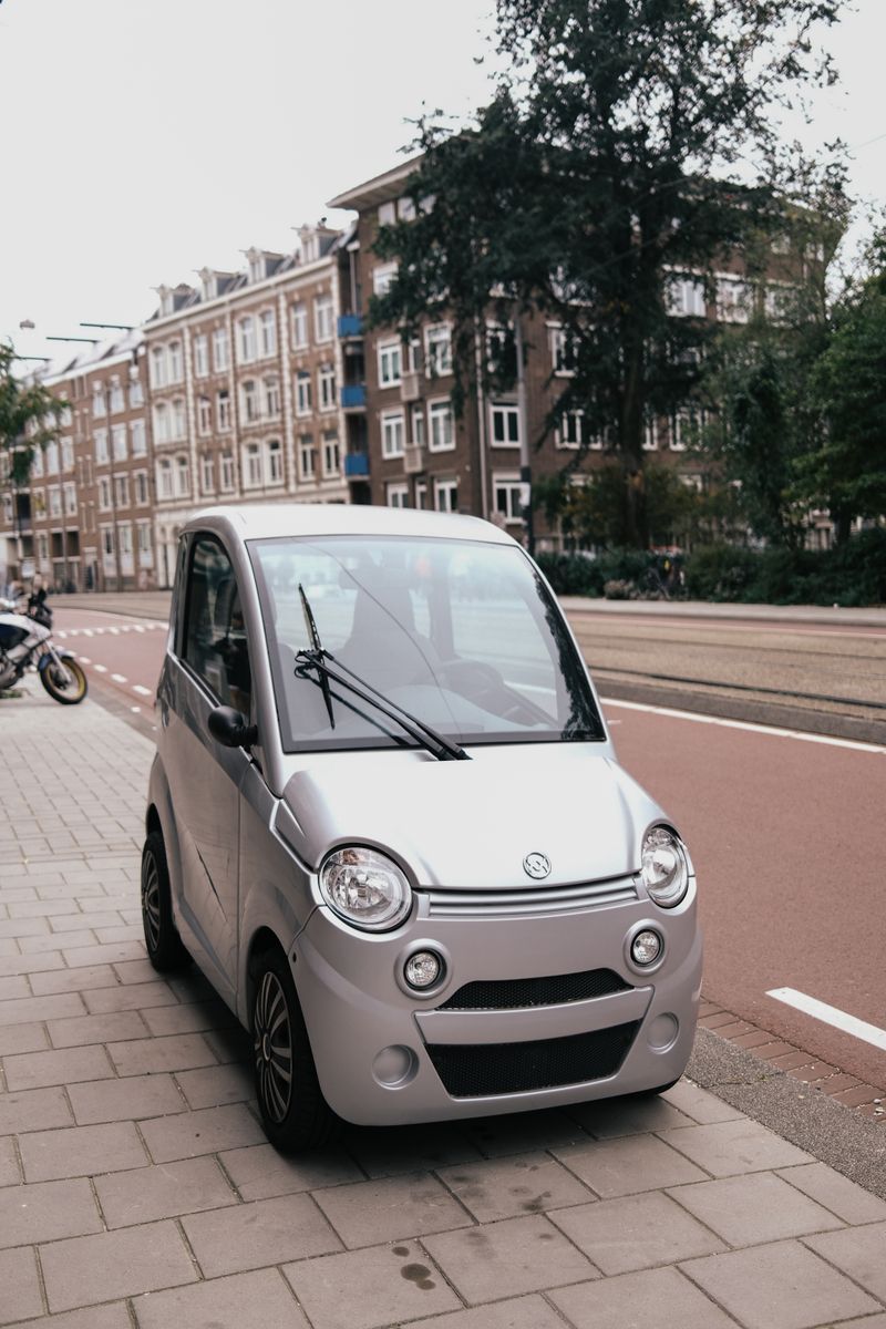 A silver electric micro-car parked on a brick sidewalk in a European city, an example of the compact EVs the Smart #2 targets