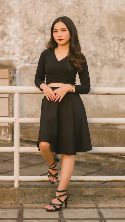 Free Fashionable woman in a black dress posing by a railing in an urban setting. Sophisticated style. Stock Photo