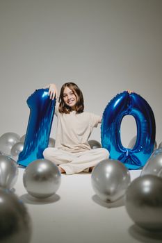 A joyful girl celebrating her 10th birthday with blue and silver balloons in a studio setting.