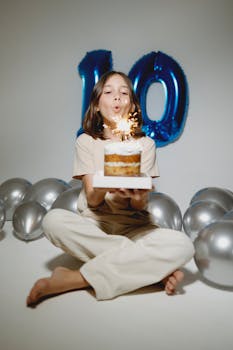A cheerful child celebrates indoors with a birthday cake and balloons.