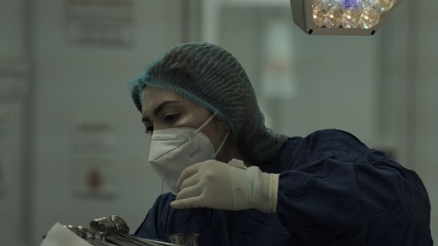 A female surgeon in full protective gear carefully performing surgery under bright surgical lights.