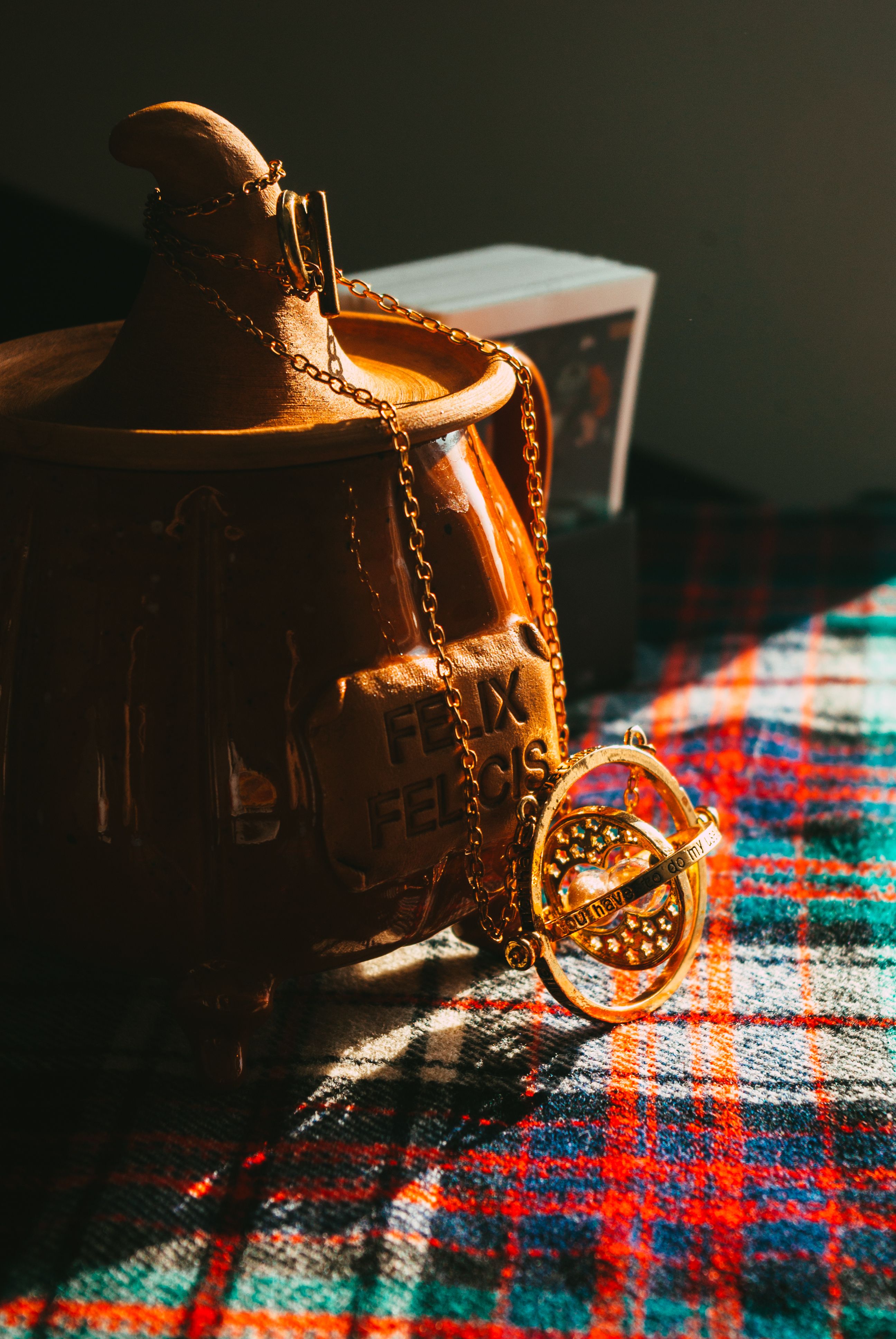 A rustic jug and gold necklace rest on a plaid cloth under warm lighting.