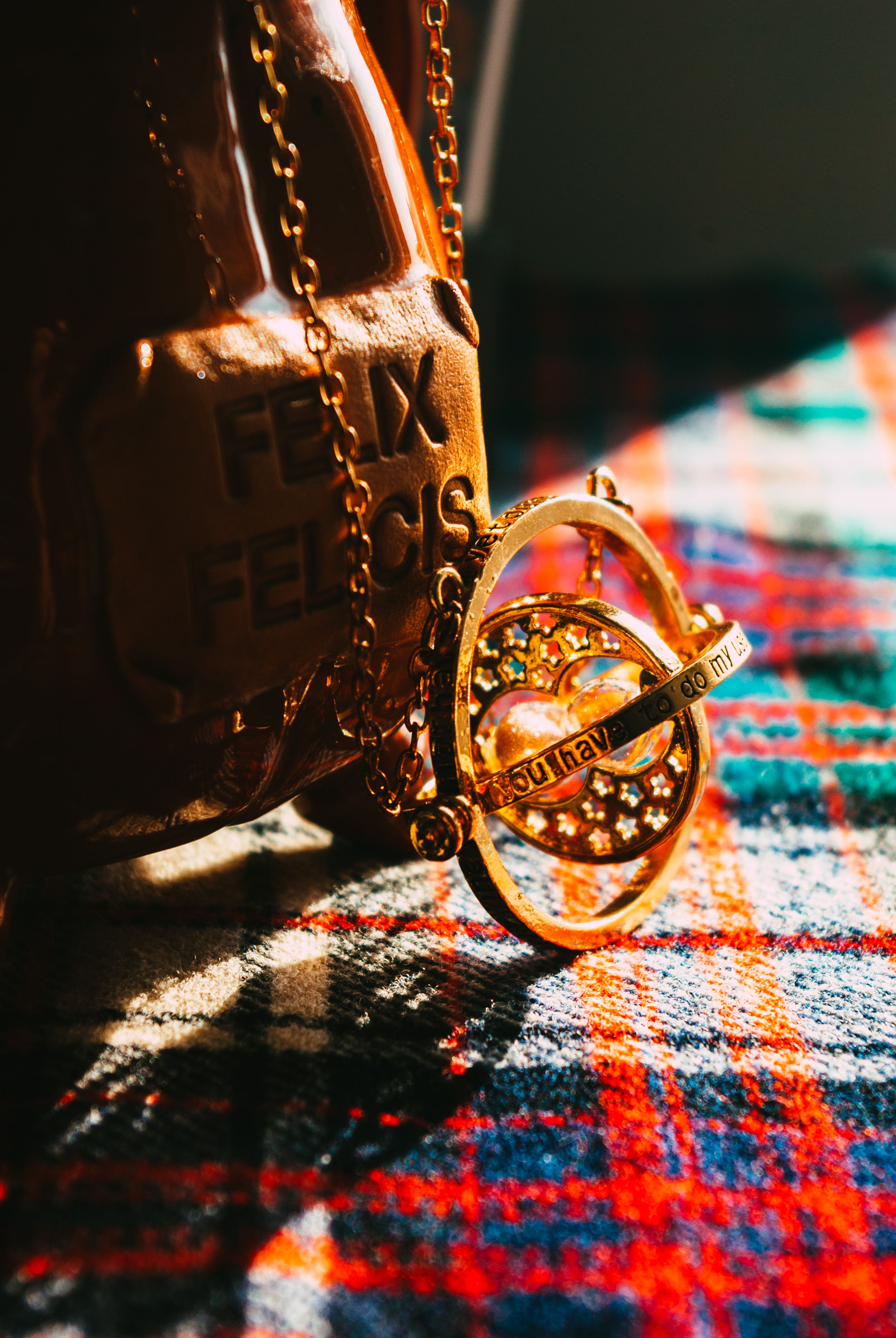 Close-up of a golden time turner necklace over plaid fabric with rich lighting.