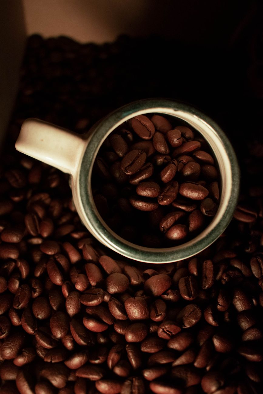 A bag of coffee and a ceramic mug on a sunlit linen-covered table