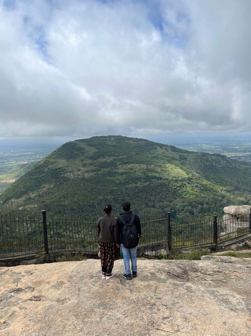 Free A couple stands on a hilltop overlooking a lush landscape under a cloudy sky. Stock Photo