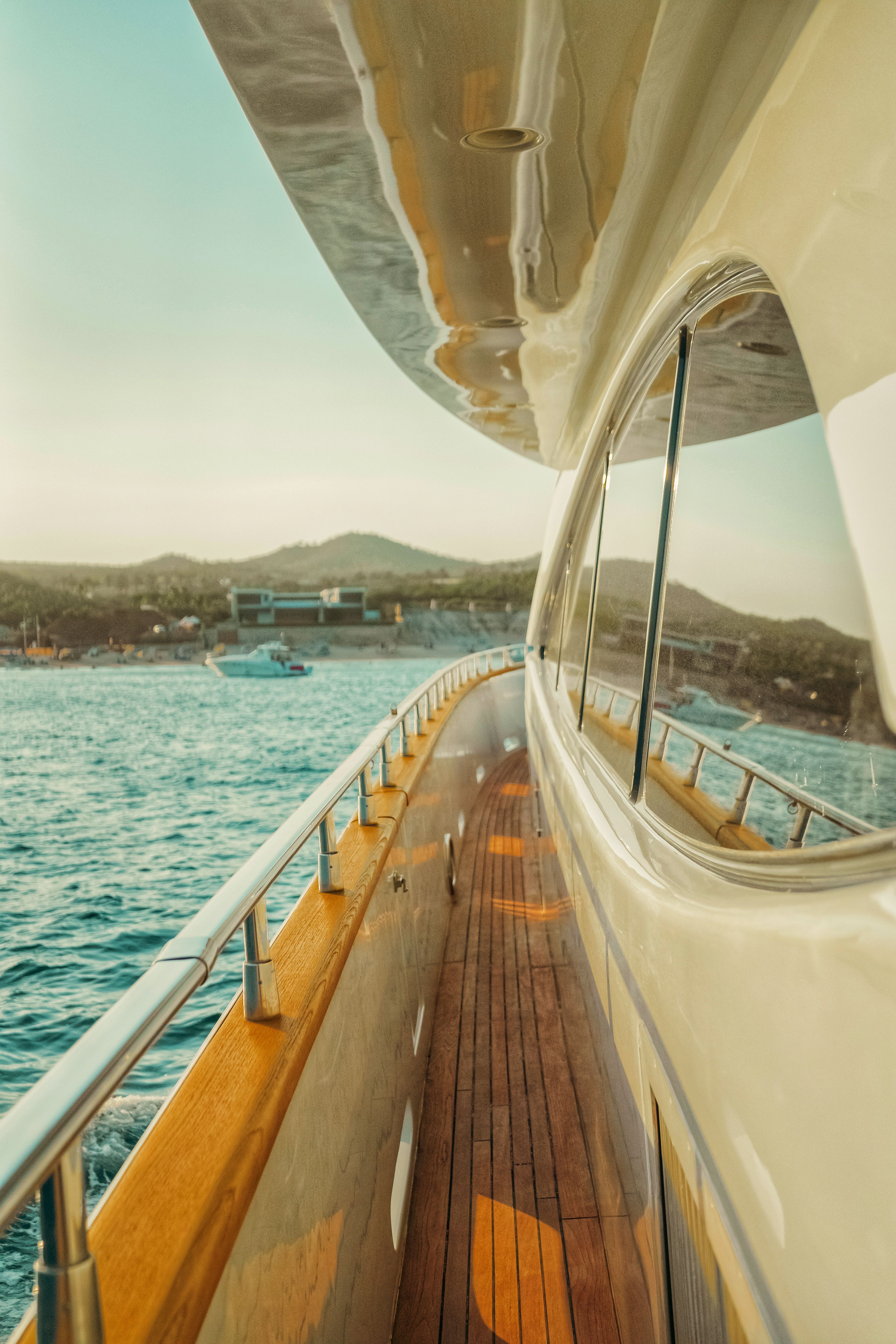 View along the teak deck of a motor yacht cruising near the shoreline on a sunny day.