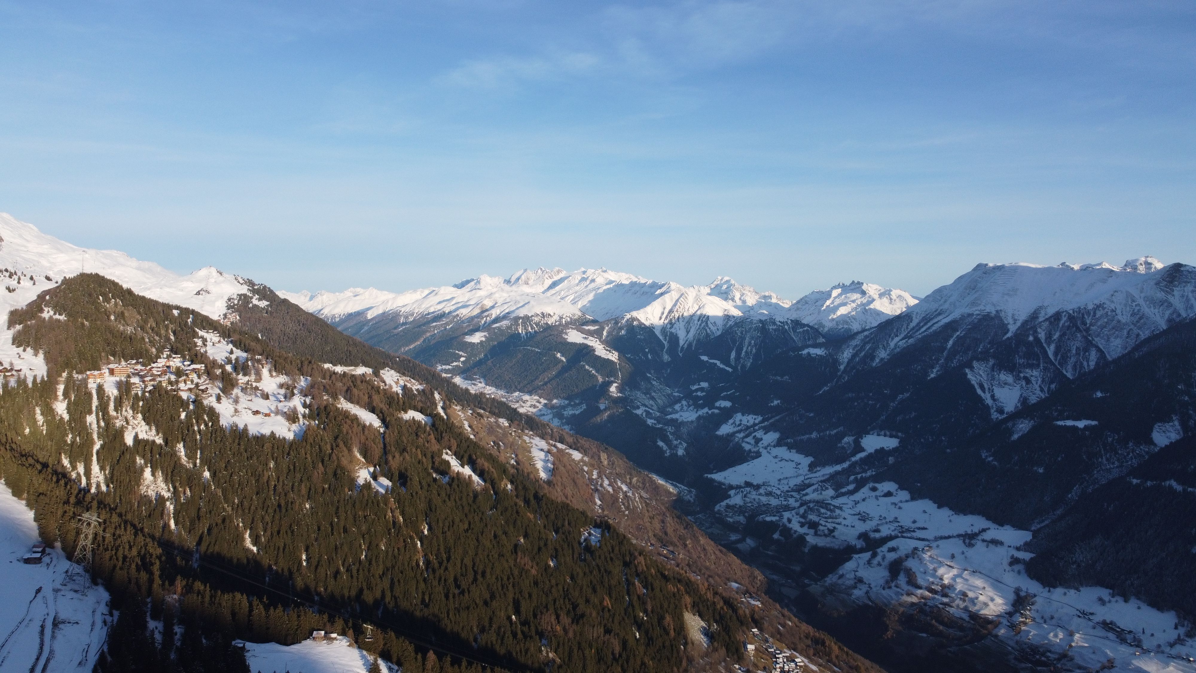 A Swiss valley in winter with a hamlet on a forested spur and a line of snow-covered peaks behind