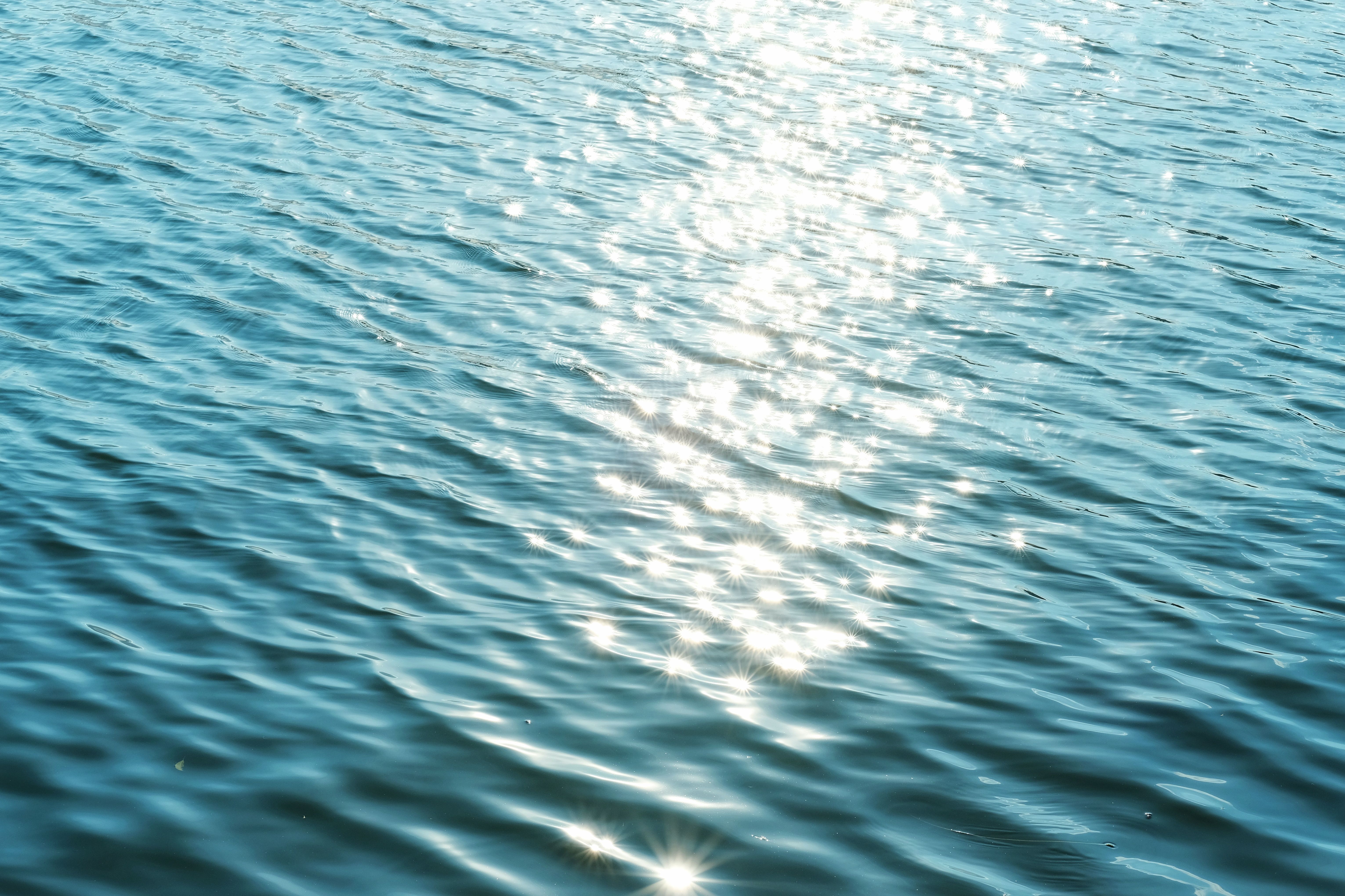 Bright sunlight creating shimmering reflections on calm ocean water surface.