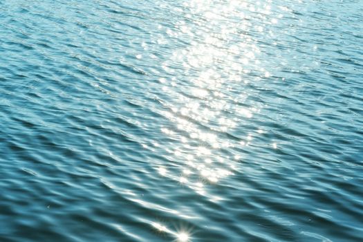 Bright sunlight creating shimmering reflections on calm ocean water surface.