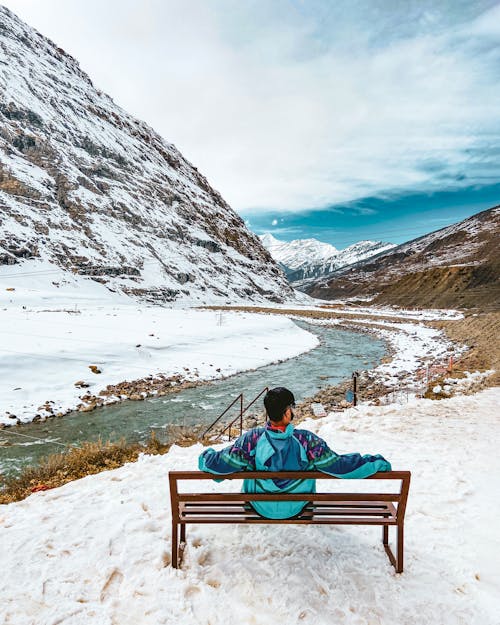 Hiker Resting on the Snow-covered Bank of a Mountain Stream