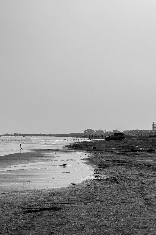Free Serene black and white photo of a coastline with an off-road vehicle by the sea. Stock Photo