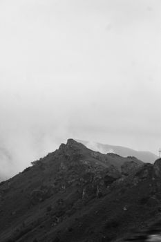 A striking monochromatic view of a rugged mountain peak with atmospheric clouds.