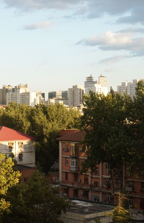 Free A scenic urban skyline with trees and diverse buildings under a dramatic sunset sky. Stock Photo