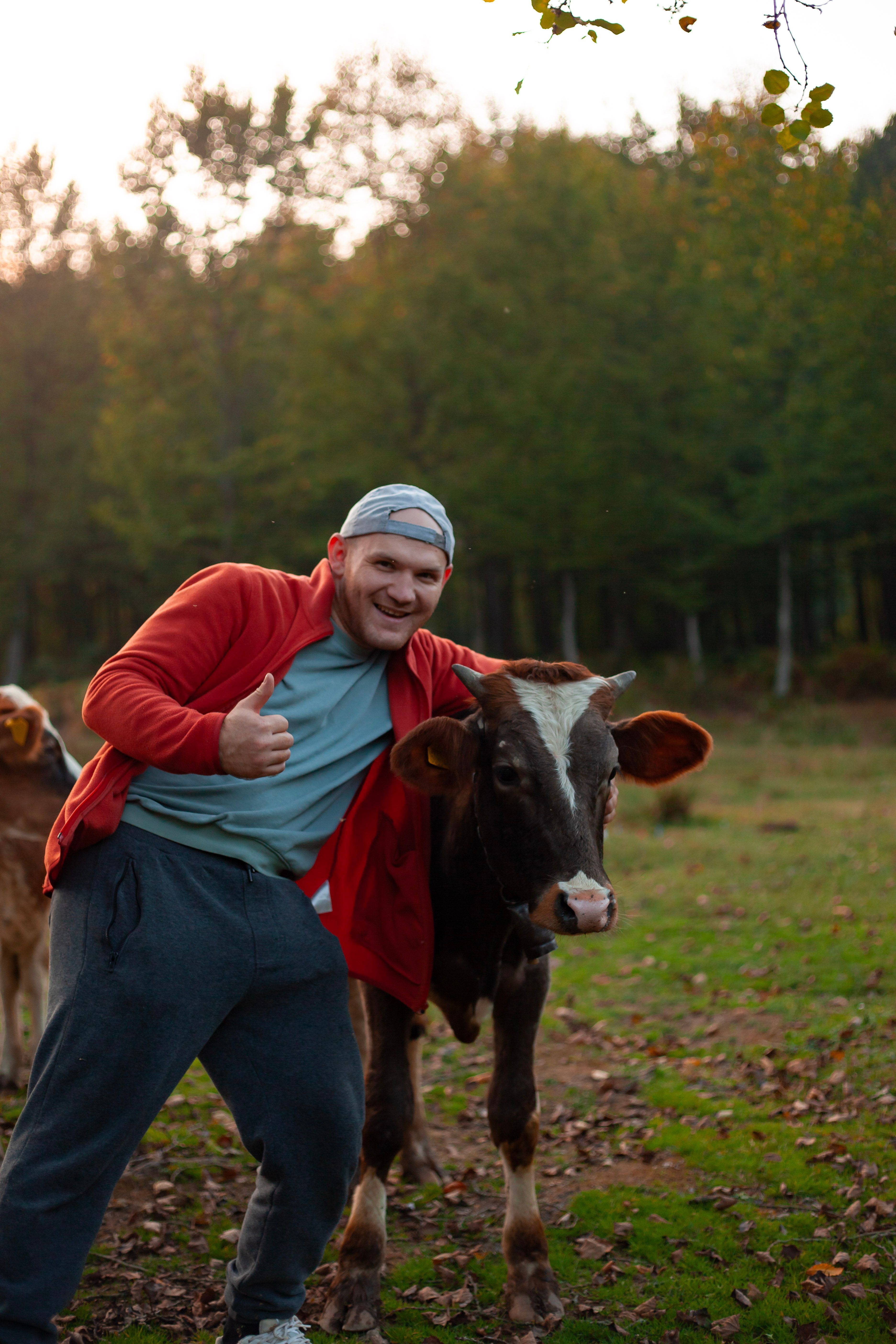 A cheerful man embraces a calf in a rural setting, showcasing livestock in a natural environment.