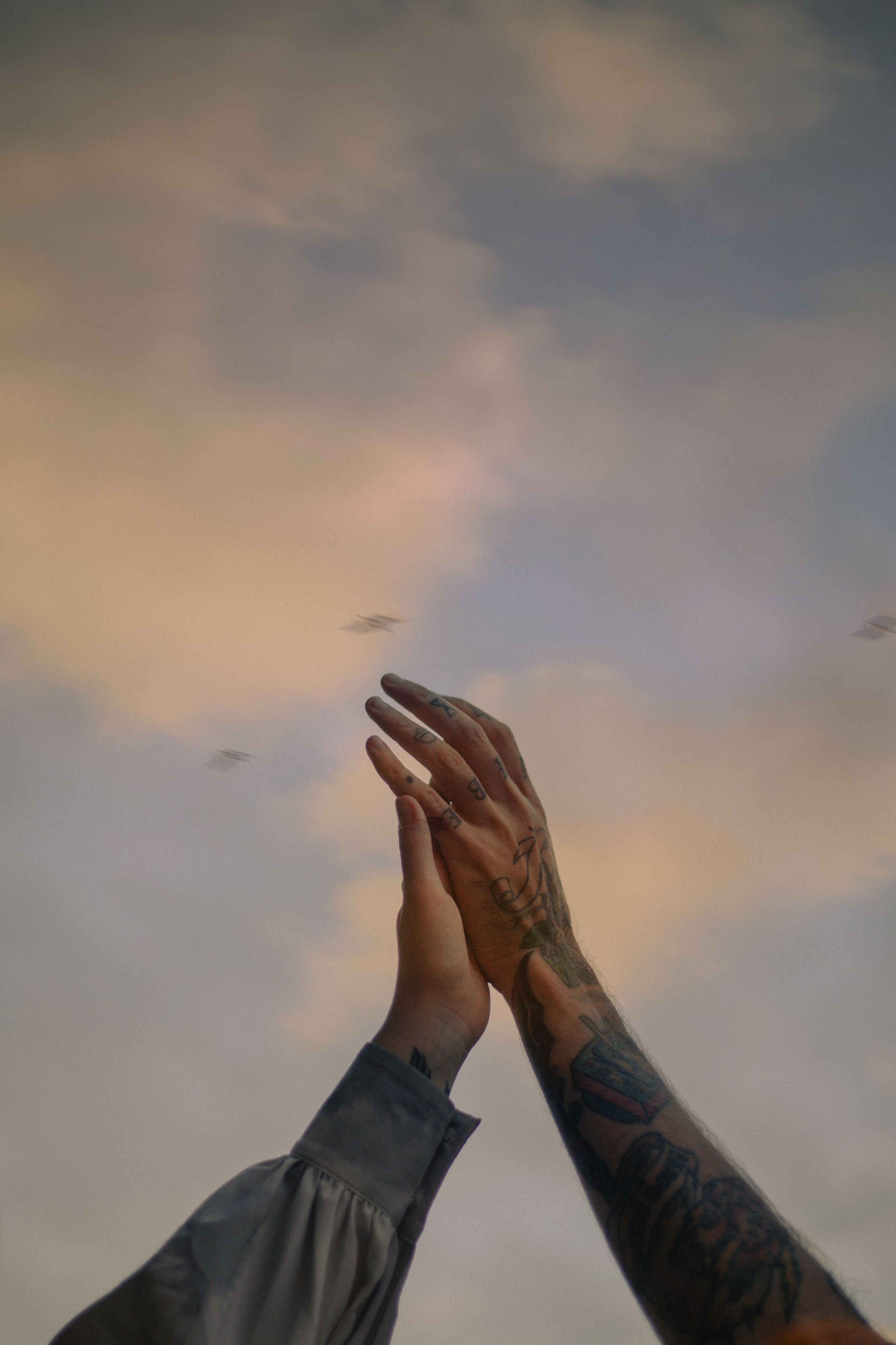 Tattooed arms and hands raised against a soft, cloudy Kyiv sky. Expressive and artistic.