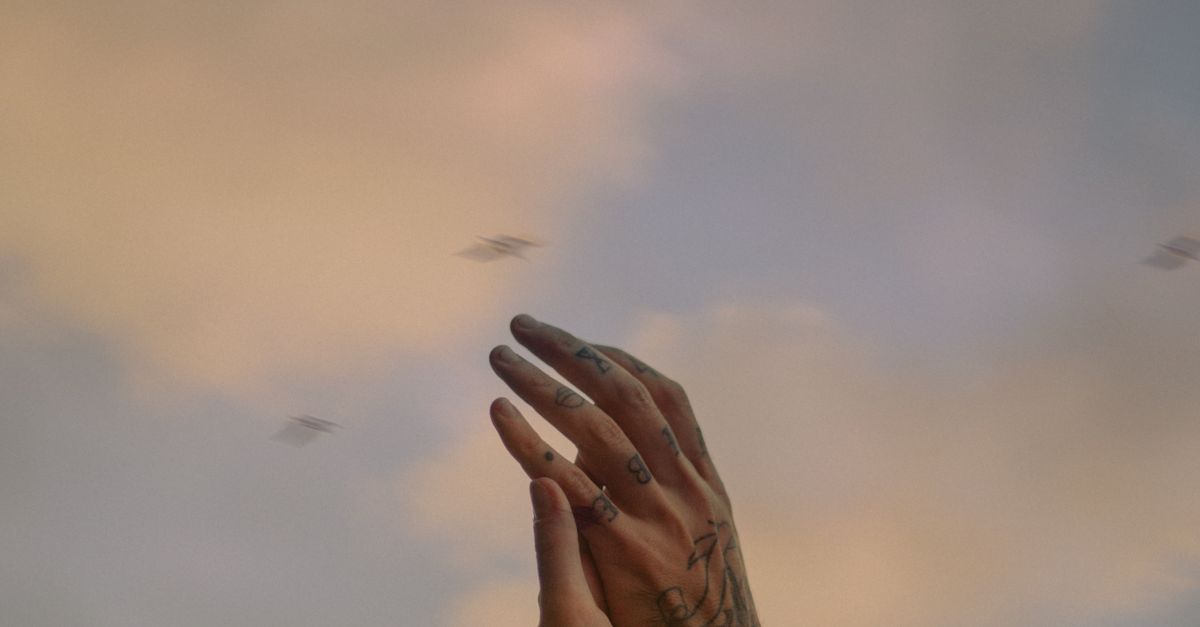 Tattooed arms and hands raised against a soft, cloudy Kyiv sky. Expressive and artistic.