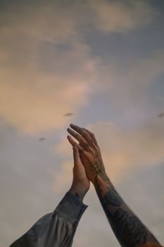 Tattooed arms and hands raised against a soft, cloudy Kyiv sky. Expressive and artistic.