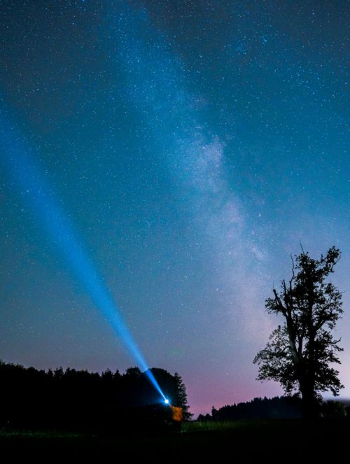 Free A stunning night sky full of stars with a silhouette and a light beam pointing upward. Stock Photo