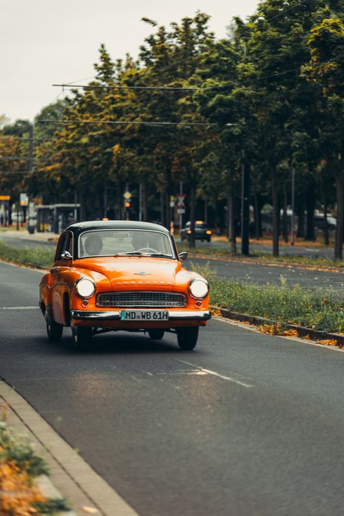 Free A classic orange car cruising a scenic tree-lined street in Magdeburg, Germany. Stock Photo