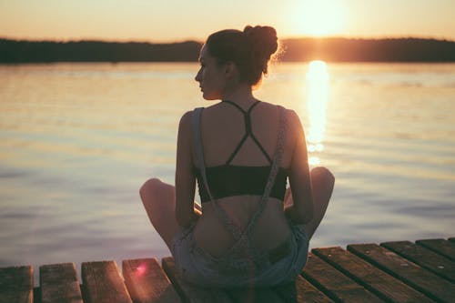 Free Woman Siting on Dock Near Large Body of Water Stock Photo