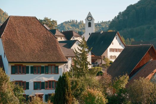 Charming European village with traditional buildings, a clock tower, and lush greenery.