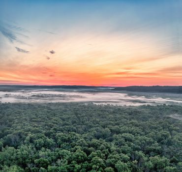 A stunning aerial view of Trevino, WI forests at sunset, enveloped in morning mist.