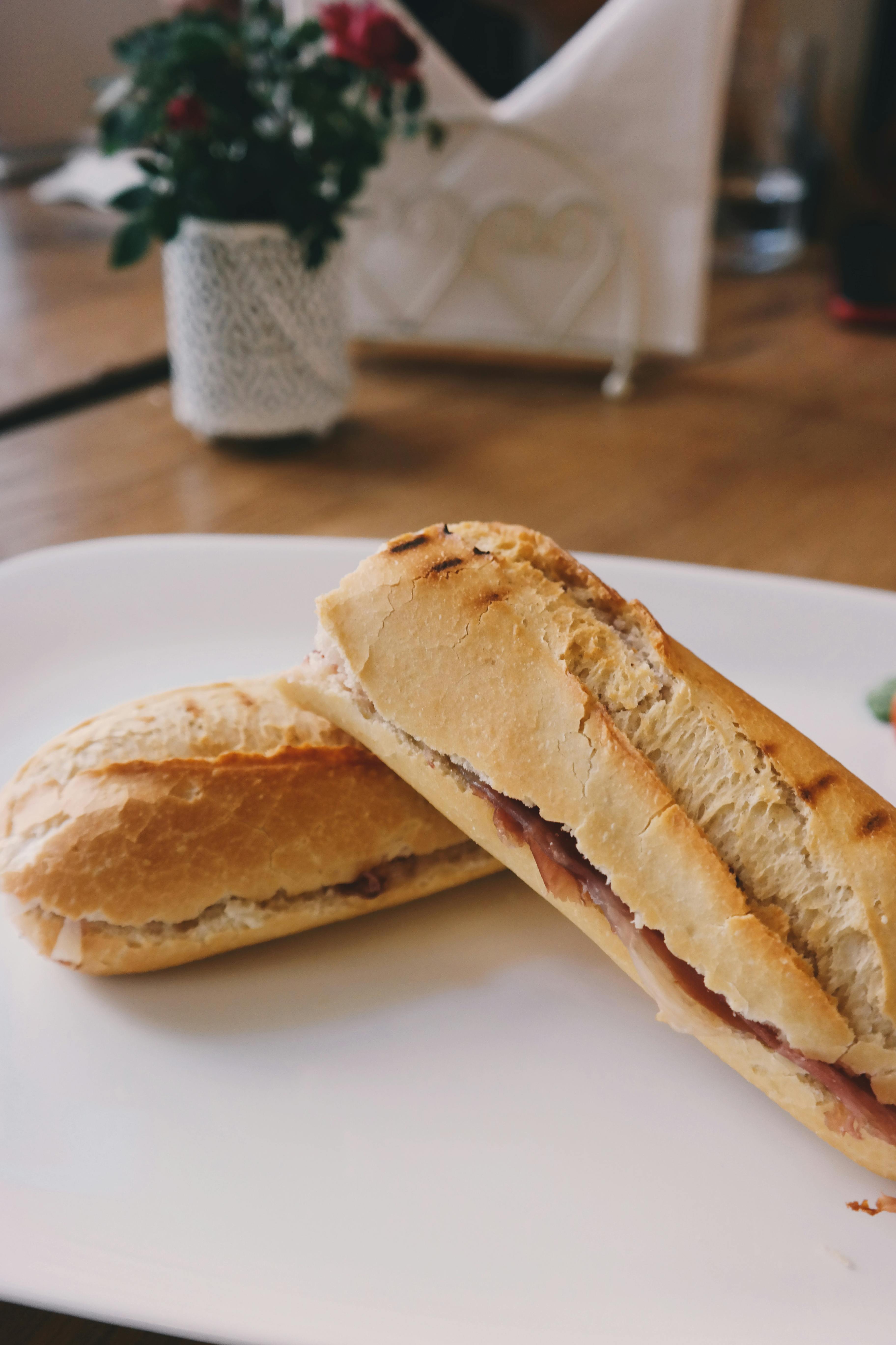 Brigitte Tohm - Delicious baguette sandwich with ham served on a white plate in a cozy setting.