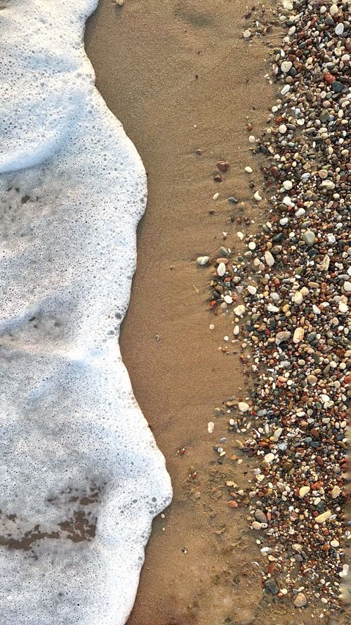Free Gentle wave washing over pebbly beach shore in a serene coastal scene. Stock Photo