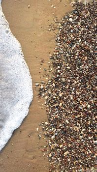 Detailed view of pebbles and sea foam meeting on a sandy beach shore.