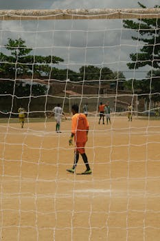 Outdoor soccer game on a sandy field in Paudalho, Brazil featuring local players.