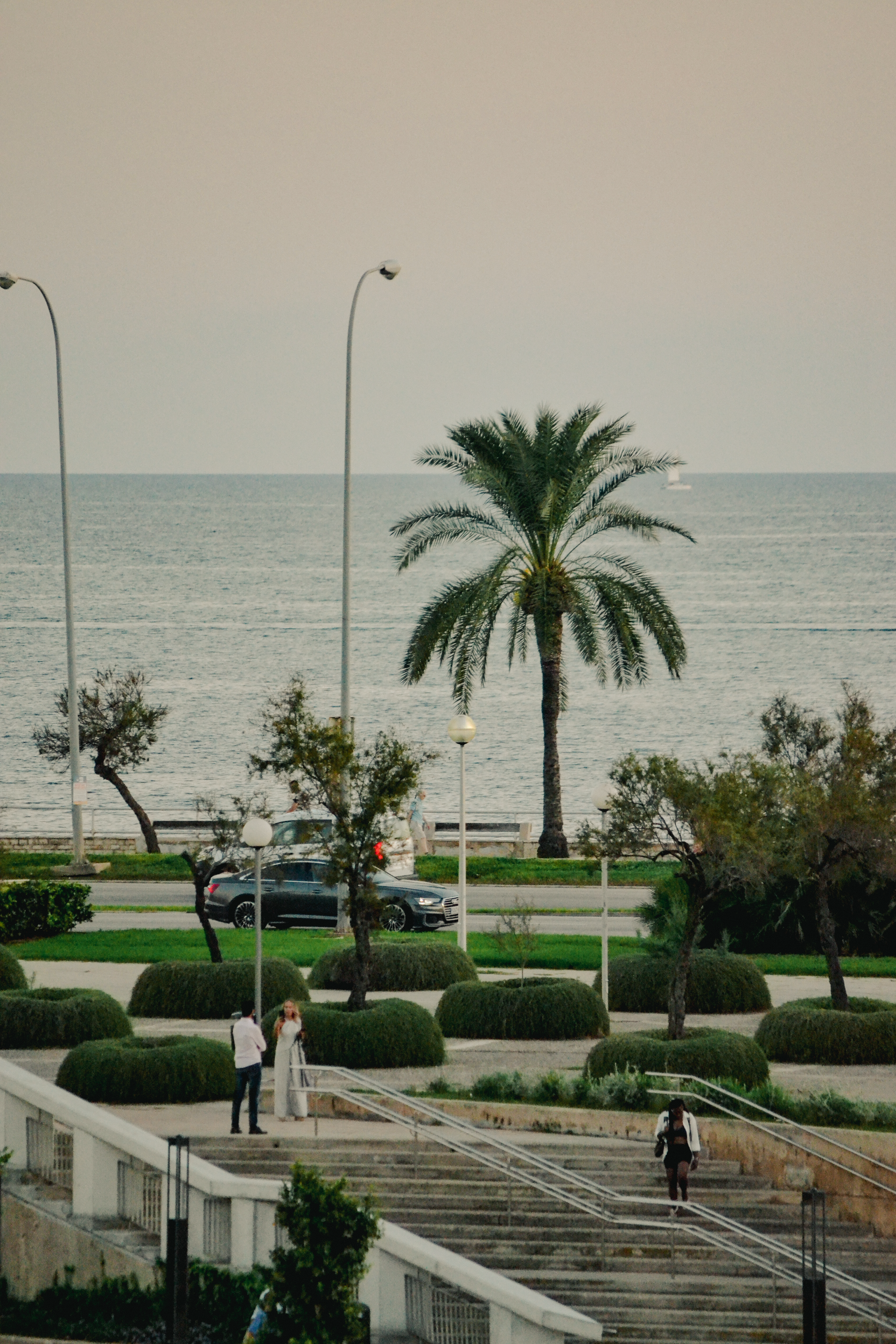 A serene view of the coastline in Spain featuring palm trees and people strolling.