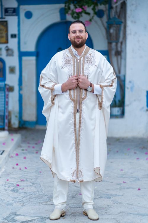 Free A smiling man in a traditional white kaftan stands confidently outdoors, showcasing cultural fashion. Stock Photo
