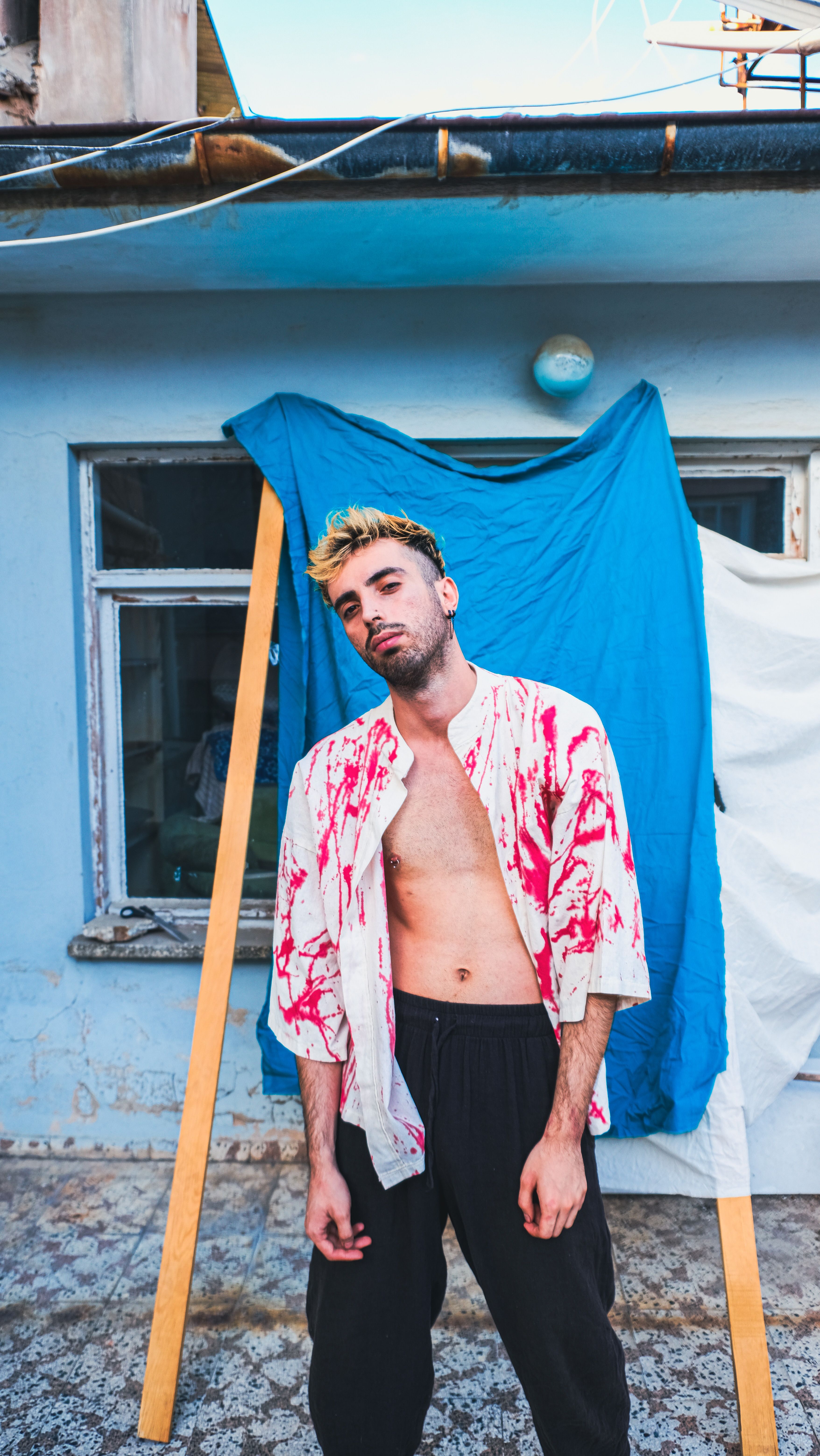 Trendy portrait of a stylish man with dyed hair standing outdoors in a fashionable outfit.